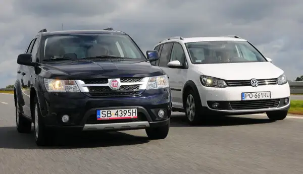 Dwa duże samochody rodzinne, ciemny Fiat i biały Volkswagen, jadą obok siebie po drodze.