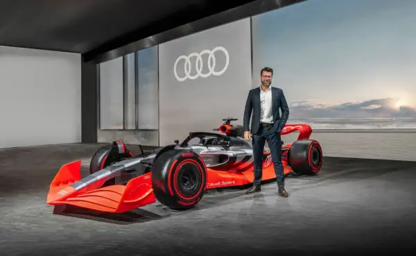 Mężczyzna w garniturze obok futurystycznego bolidu Audi F1 2026.