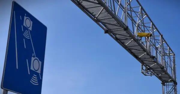 Niebieski znak informuje o odcinkowym pomiarze prędkości S7. Żółta kamera zamontowana na konstrukcji nad drogą rejestruje pojazdy.