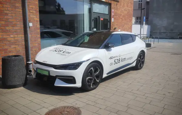Biały samochód elektryczny Kia z napisem "#GOelectric D do 528 km zasięgu" informuje, ile prądu zużywa samochód elektryczny.