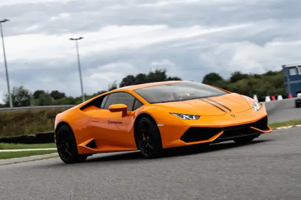 Pomarańczowe Lamborghini z czarnymi pasami na masce podczas szybkiego przejazdu po torze wyścigowym.