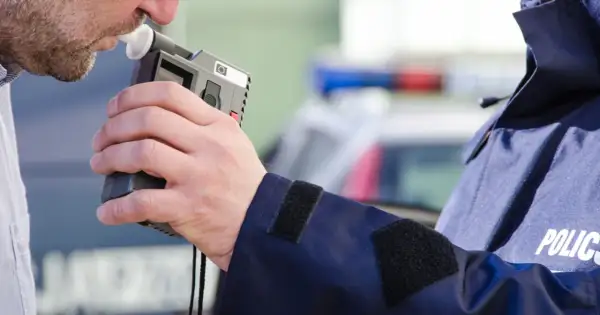 Mężczyzna dmucha w alkomat, który pokazuje wynik, mimo że nie pił. Policjant w mundurze z napisem POLICJA trzyma urządzenie.