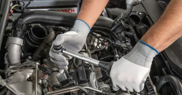 Mechanik w białych rękawiczkach dokonuje precyzyjnej wymiany świec w silniku samochodu, używając klucza dynamometrycznego.