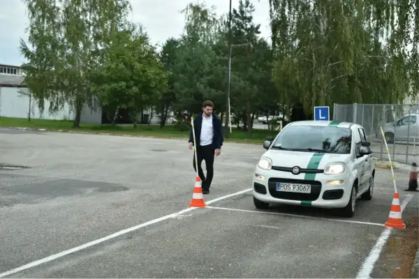 Egzaminator ustawia pachołek, a kursant wykonuje hamowanie awaryjne na placu manewrowym.