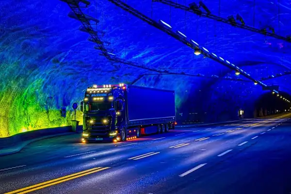 Ciężarówka jedzie przez najdłuższy tunel drogowy na świecie, oświetlony niebieskim i zielonym światłem.