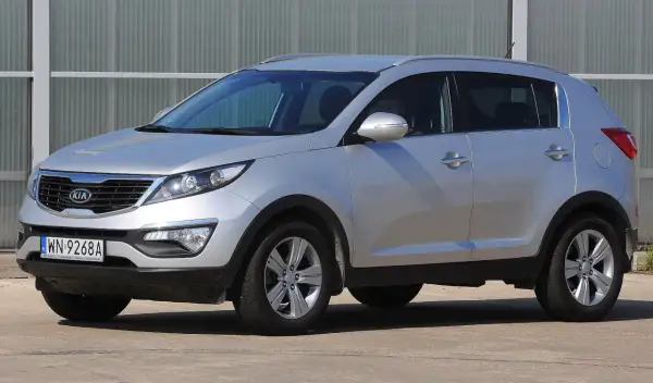 Srebrny Kia Sportage, jeden z najmniej awaryjnych aut terenowych, zaparkowany przed budynkiem.