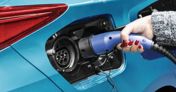 Dłoń z czerwonym lakierem na paznokciach podłącza ładowarkę do samochodu plug-in hybryda.